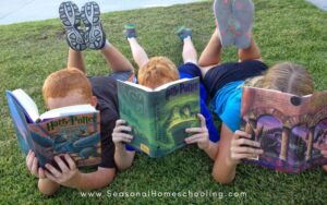 3 kids laying on their stomachs in the grass reading Harry Potter books