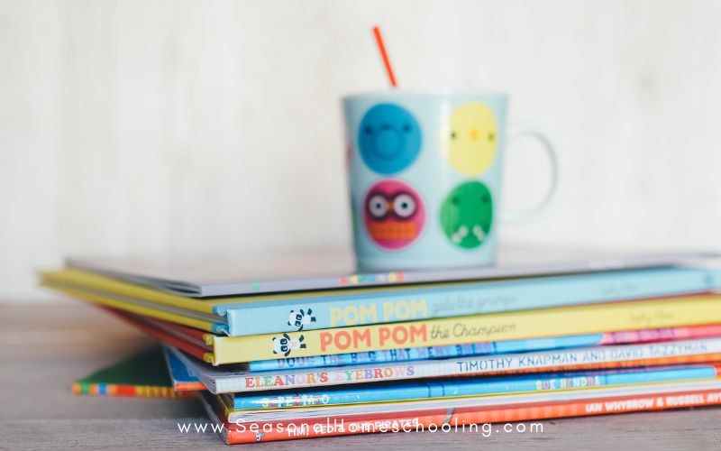 children's books stacked on desk with smiley face cup beside it